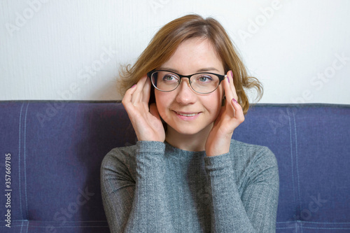 Portrait of a young smiling woman with glasses on the sofa.