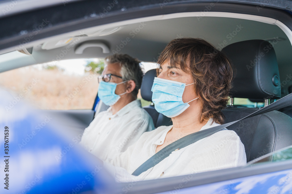 New normal. Female driver with a medical face mask driving a car with a passenger. Health protection. Family in the car protected by a mask safety and pandemic concept. Coronavirus. Social distance. New normal. Female driver with a medical face mask driving a car with a passenger. Health protection. Family in the car protected by a mask safety and pandemic concept. Coronavirus. Social distance.