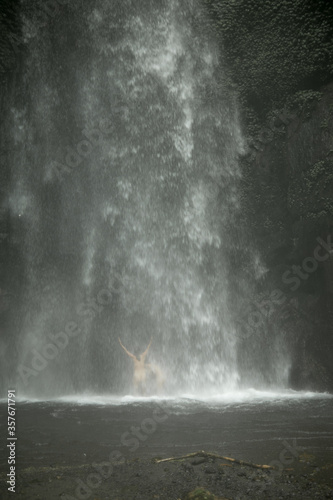 One of the largest waterfalls on the Bali island. Naked woman into a waterfall in the Kintamani area near the volcano. Hiking to the beautiful waterfall. Image with selective focus.