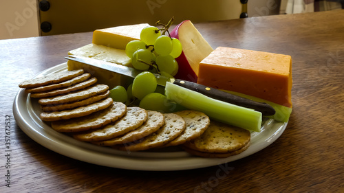 Rustic platter of crackers, knife and varied assortment of traditional cheeses, complemented with green grapes and celery. Set on an oak table. Interior image in natural light.