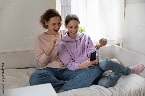 Tableau sur toile Happy Caucasian mom and teen daughter sit relax on bed at home have fun using ce