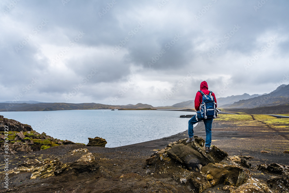 Obraz premium Man hiking in Iceland standing on the peak of rocks with backpack looking at the stunning view near the Kleifarvatn lake in Reykjanesfólkvangur nature reserve park