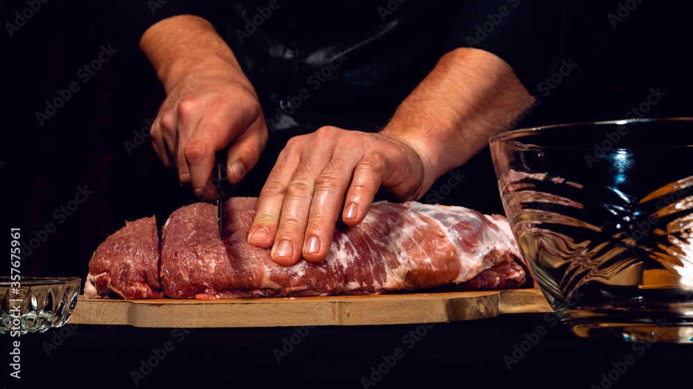 The chef of the restaurant in a dark uniform cuts the meat with a black kitchen knife. Preparation of pork marinated steak to order.