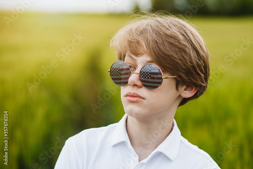Boy walking with the american flag on the green wheat field celebrating national independence day. 4th of July concept.