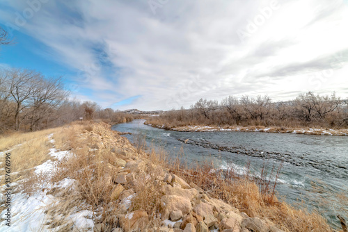 Scenic river with snowy shore against distant hills under cloudy sky in winter