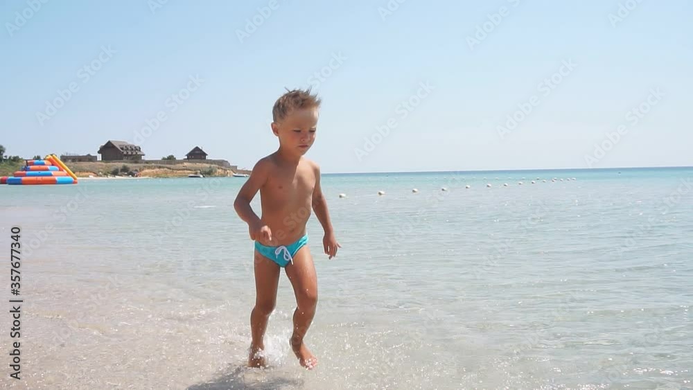Happy baby runs across the azure sea creating splashes in different directions, slow-motion video. Happy baby runs across the azure sea creating splashes in different directions, slow-motion video.