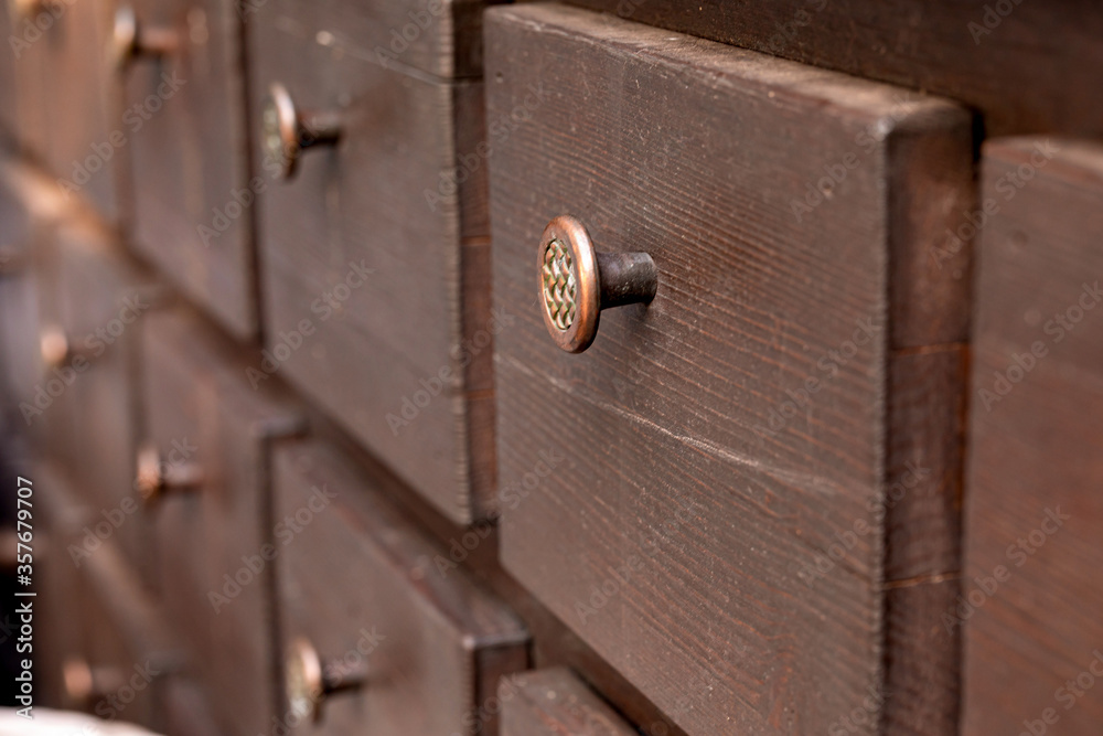 Obraz premium Wooden chest of drawers with small drawers and round brass handles for storing buttons, jewelry, and jewelry. Historic element of an interior