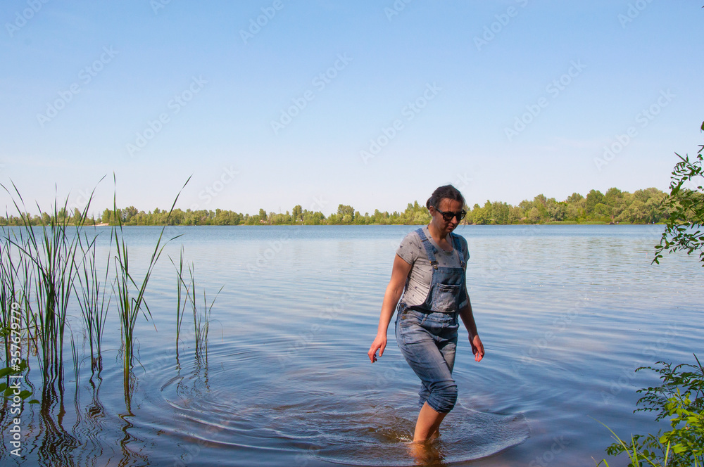 Girl in denim overalls goes in the water in the river