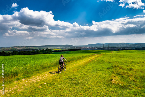 Photography Man Rides Mountainbike In Rural Landscape In Front Of Skyline Of Vienna In Austr