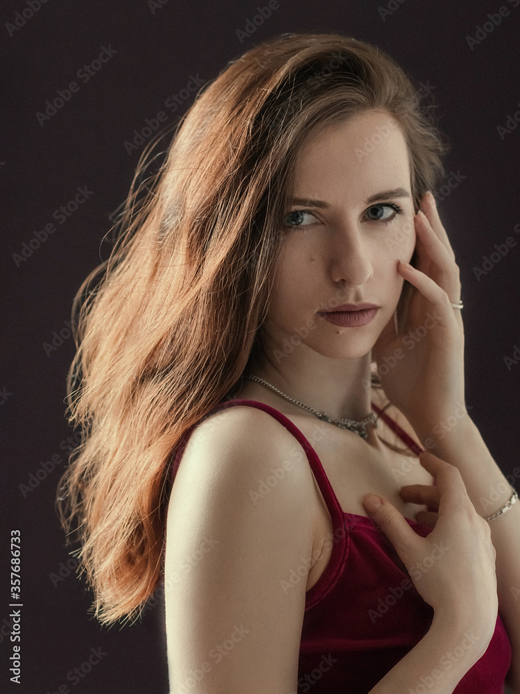 Obraz premium Portrait of a beautiful young girl. The girl stands and gently touches her face with her hands. Dramatic portrait. The light of the sun in the hair.