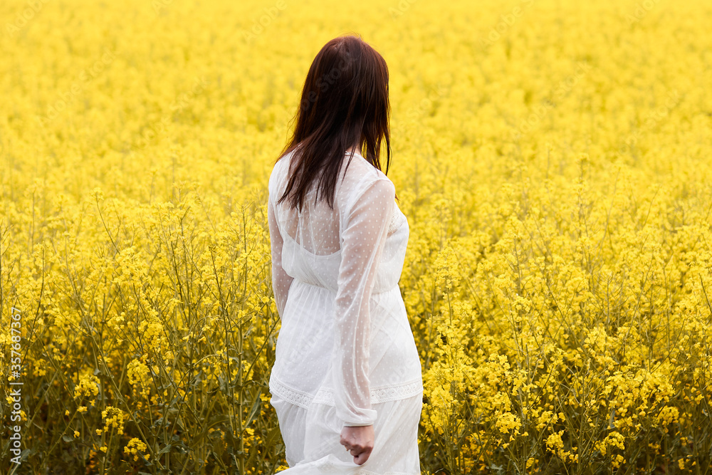 Woman in a white dress standing back in a yellow rapeseed field. Spring concept. Woman in a white dress standing back in a yellow rapeseed field. Spring concept.