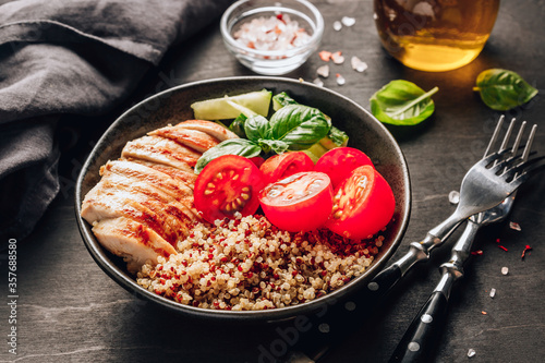 Healthy salad bowl with quinoa, tomatoes, chicken, cucumber and basil on black wooden background. Superfoods.