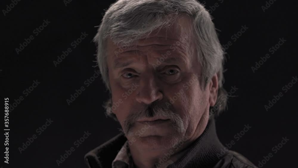 Super close up of senior grey haired man looking at camera and nod head wearing jacket in semi lit light studio isolated on black background. Prores 422. Super close up of senior grey haired man looking at camera and nod head wearing jacket in semi lit light studio isolated on black background. Prores 422.