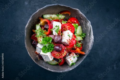 Traditioneller griechischer Bauernsalat mit Tomaten, Oliven und Feta Käse angeboten als Draufsicht in einer rustikalen Modern Design Schale