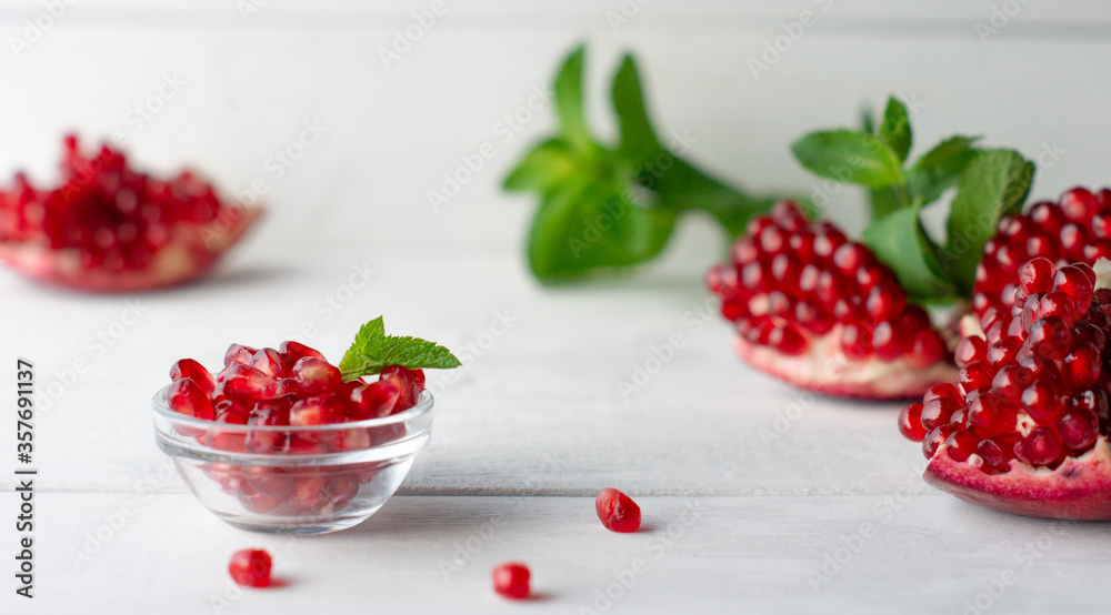 Pomegranate grains in a glass cup, pomegranate and fresh mint on white boards Pomegranate grains in a glass cup, pomegranate and fresh mint on white boards