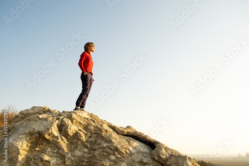 Young woman hiker standing alone on big stone in morning mountains. Female tourist on high rock in wild nature. Tourism  traveling and healthy lifestyle concept.