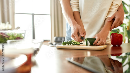 Cropped shot of woman cutting vegetables while man helping  holding her hands  standing behind her. Vegetarians preparing healthy meal in the kitchen together