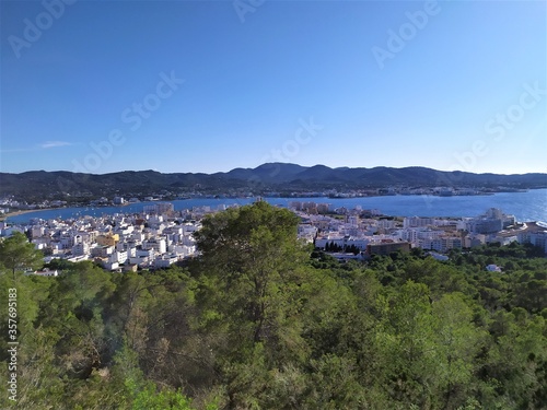 View of San Antonio harbor from wooded hills  sea and mountains in background  houses and hotels in San Antonio  Ibiza  photo