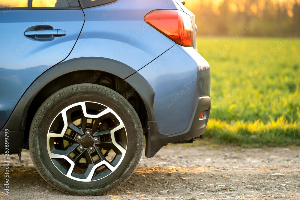 Close up of blue off road car wheel on gravel road. Traveling by auto, adventure in wildlife, expedition or extreme travel on a SUV automobile. Offroad 4x4 vehicle in field at sunrise.