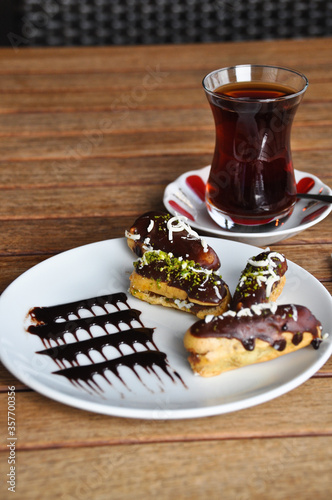 Tiny cakes in white plate on wooden table, black tea next to it, ekler pastry photo