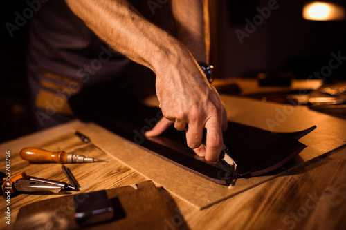 Working process of the leather belt in the leather workshop. Man holding crafting tool and working. Tanner in old tannery. Wooden table background