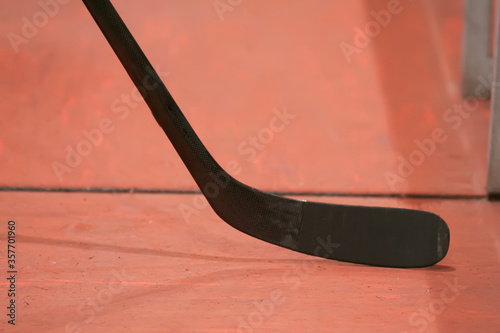 Closeup of an black ice hockey stick against light red background.