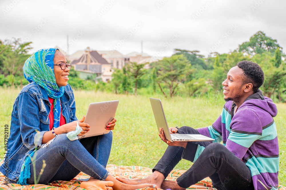 young black people, using their laptop computer, sitting together in a park, students working together, discussing a project