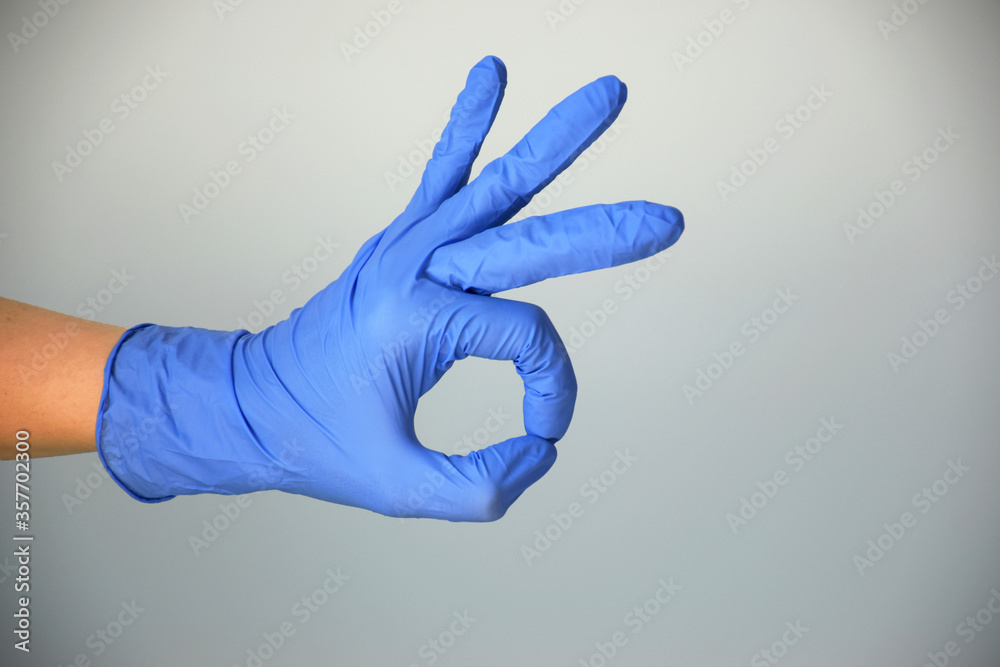 Hand in blue rubber protective glove isolated on gray gesturing okay, normal, well, positive. Sign language, kitchen gloves, cleaning gloves. Copy space. Hand in blue rubber protective glove isolated on gray gesturing okay, normal, well, positive. Sign language, kitchen gloves, cleaning gloves. Copy space.
