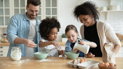 Full multi ethnic family with adorable daughters gathered in modern kitchen cooking pancakes together. Cake mix preparation, make yummy home-made dessert, enjoy communication and cookery hobby concept