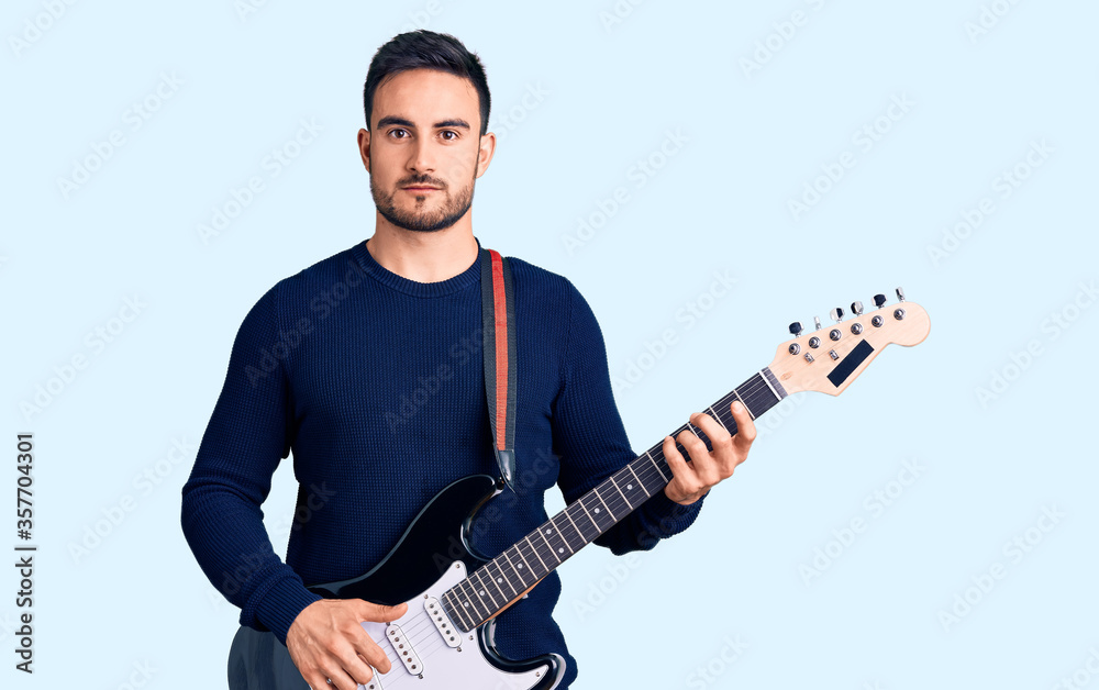 Young handsome man playing electric guitar thinking attitude and sober expression looking self confident