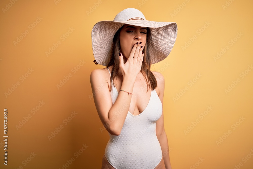Young beautiful brunette woman on vacation wearing swimsuit and summer hat bored yawning tired covering mouth with hand. Restless and sleepiness. Young beautiful brunette woman on vacation wearing swimsuit and summer hat bored yawning tired covering mouth with hand. Restless and sleepiness.