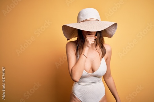 Young beautiful brunette woman on vacation wearing swimsuit and summer hat feeling unwell and coughing as symptom for cold or bronchitis. Health care concept.