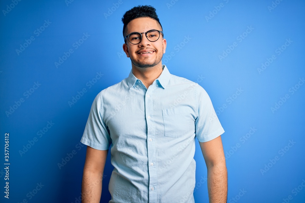 Fototapeta premium Young handsome man wearing casual summer shirt and glasses over isolated blue background with a happy and cool smile on face. Lucky person.