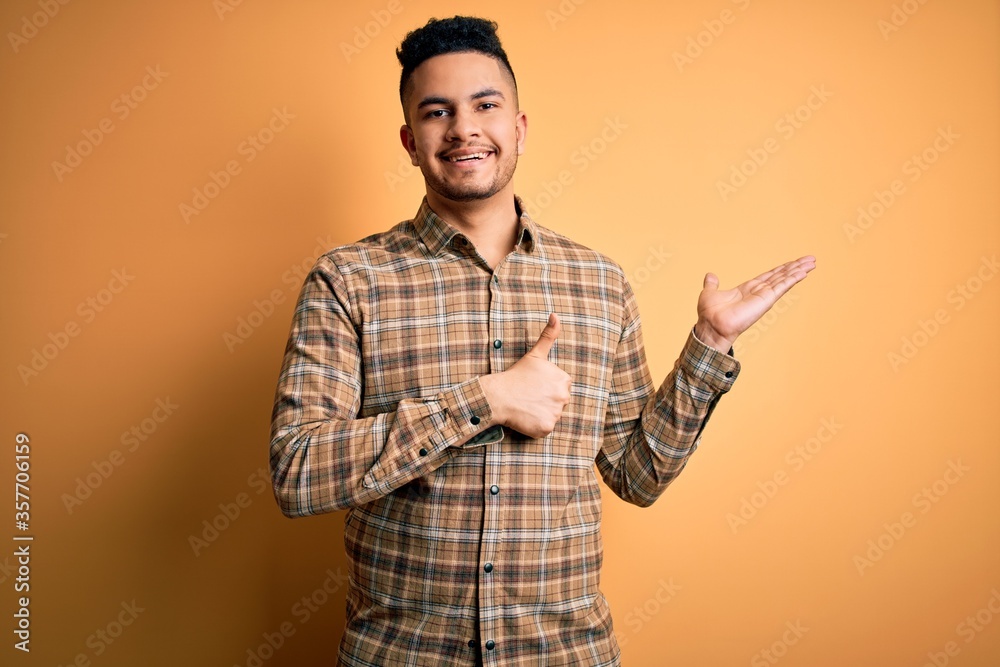 Young handsome man wearing casual shirt standing over isolated yellow background Showing palm hand and doing ok gesture with thumbs up, smiling happy and cheerful Young handsome man wearing casual shirt standing over isolated yellow background Showing palm hand and doing ok gesture with thumbs up, smiling happy and cheerful
