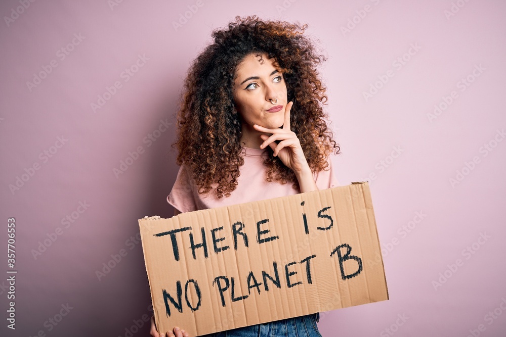 Young beautiful activist woman with curly hair and piercing protesting asking for change planet serious face thinking about question, very confused idea Young beautiful activist woman with curly hair and piercing protesting asking for change planet serious face thinking about question, very confused idea