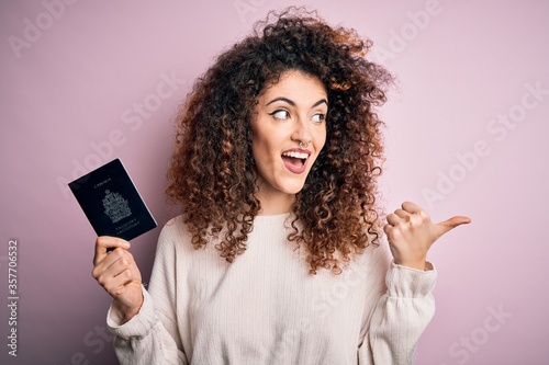 Beautiful tourist woman with curly hair and piercing holding canada canadian passport id pointing and showing with thumb up to the side with happy face smiling