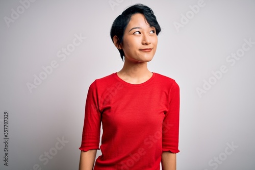 Foto Young beautiful asian girl wearing casual red t-shirt standing over isolated white background smiling looking to the side and staring away thinking
