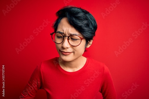 Young beautiful asian girl wearing casual t-shirt and glasses over isolated red background with hand on stomach because indigestion, painful illness feeling unwell. Ache concept.