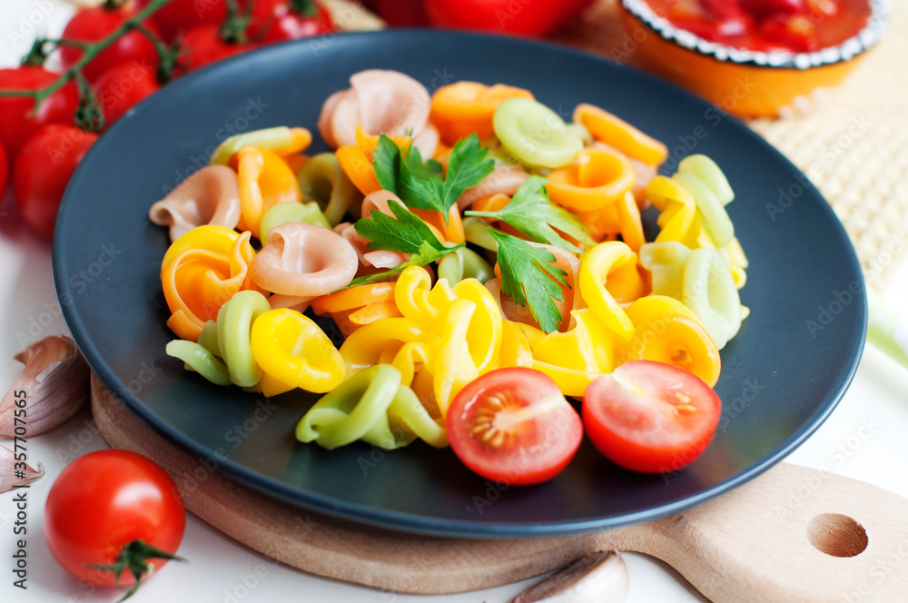 Colorful pasta with tomatoes, garlic, parsley, pepper on a black plate. Pasta for child with tomato sauce on a white background