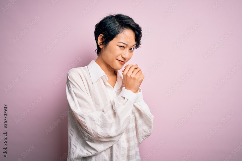 Young beautiful asian girl wearing casual shirt standing over isolated pink background laughing nervous and excited with hands on chin looking to the side Young beautiful asian girl wearing casual shirt standing over isolated pink background laughing nervous and excited with hands on chin looking to the side