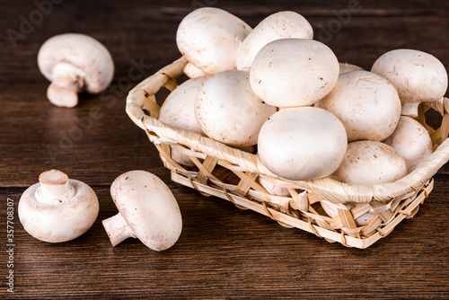 Fresh champignon mushrooms in a small basket and several on the table.