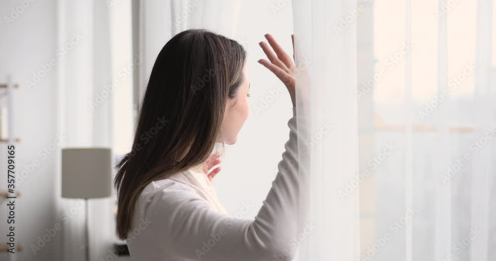 Head shot side view happy attractive millennial woman coming to window, looking out on street, admiring scenery in hotel on vacation. Smiling young lady watching cityscape, enjoying weekend time.