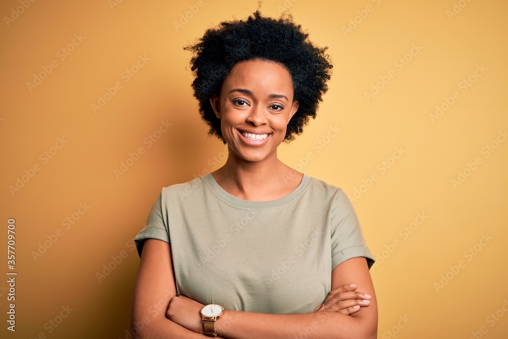 Young beautiful African American afro woman with curly hair wearing casual t-shirt happy face smiling with crossed arms looking at the camera. Positive person.