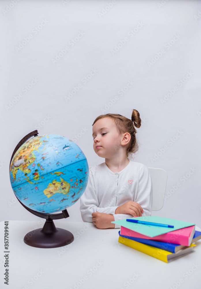 Vertical orientation. A smart girl student sits at a table and looks at a globe on a white isolated background with space for text Vertical orientation. A smart girl student sits at a table and looks at a globe on a white isolated background with space for text