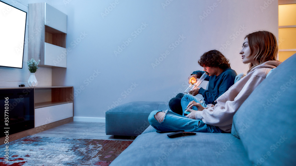 Φωτογραφία Side view of young caucasian guy lighting cannabis in the bowl of glass water pi