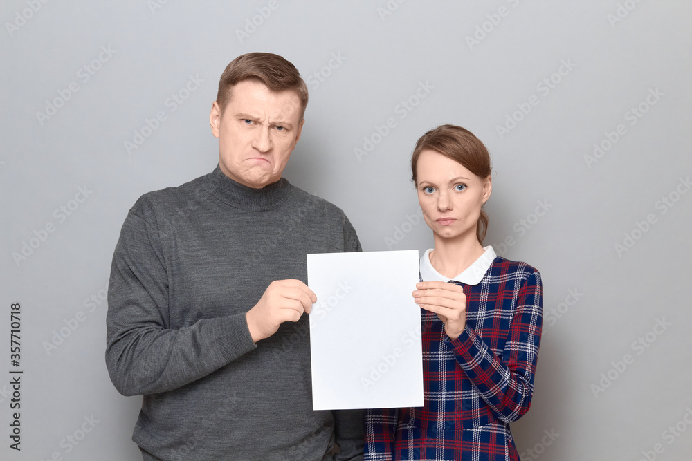 Portrait of adult couple holding together white blank paper sheet Portrait of adult couple holding together white blank paper sheet