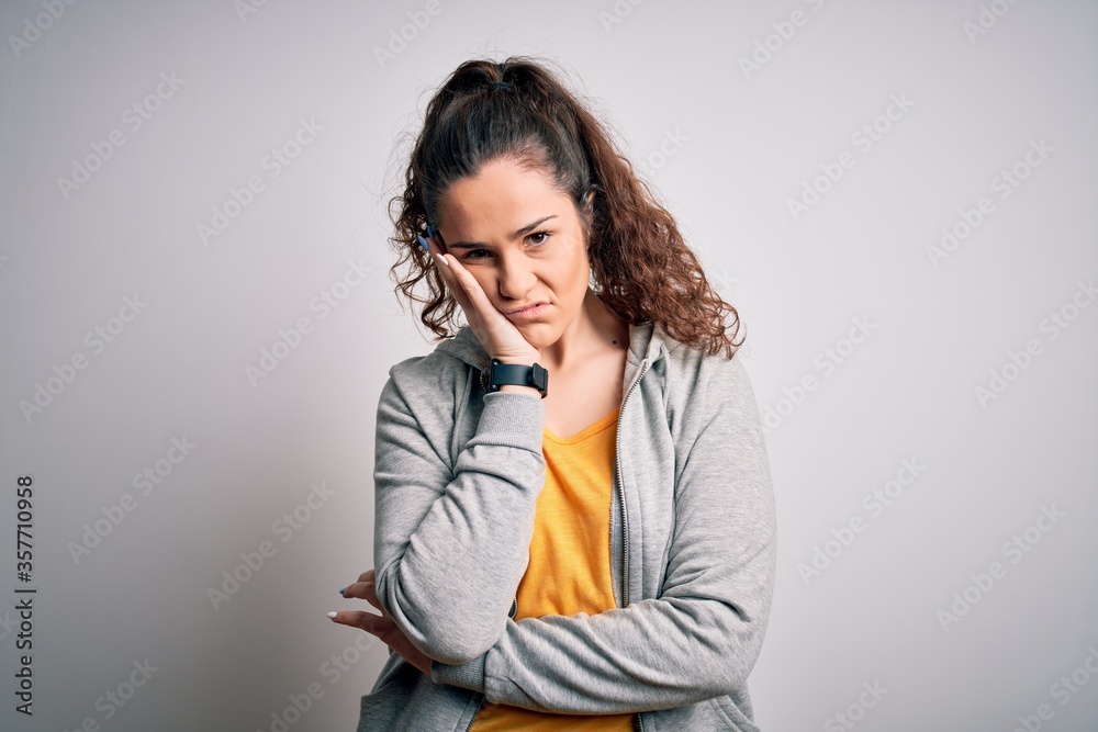 Young beautiful sportswoman with curly hair wearing sportswear over white background thinking looking tired and bored with depression problems with crossed arms. Young beautiful sportswoman with curly hair wearing sportswear over white background thinking looking tired and bored with depression problems with crossed arms.