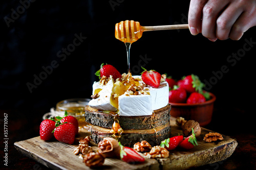 Selective focus. Camembert cheese with nuts, honey and strawberries. Honey flowing with honey stick on camembert cheese. Healthy snack. Keto diet.