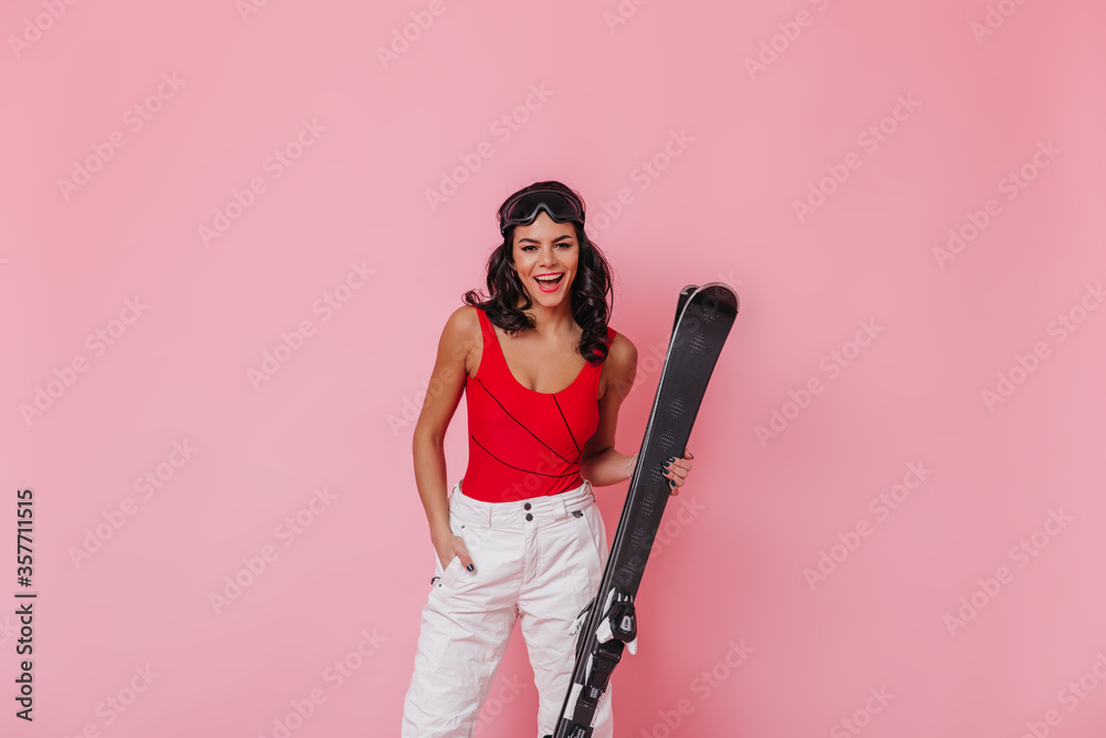 Pleasant woman holding skis. Front view of brunette girl in sport goggles. Pleasant woman holding skis. Front view of brunette girl in sport goggles.