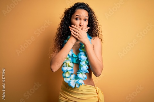 Young beautiful american woman on vacation wearing bikini and hawaiian lei flowers shocked covering mouth with hands for mistake. Secret concept.